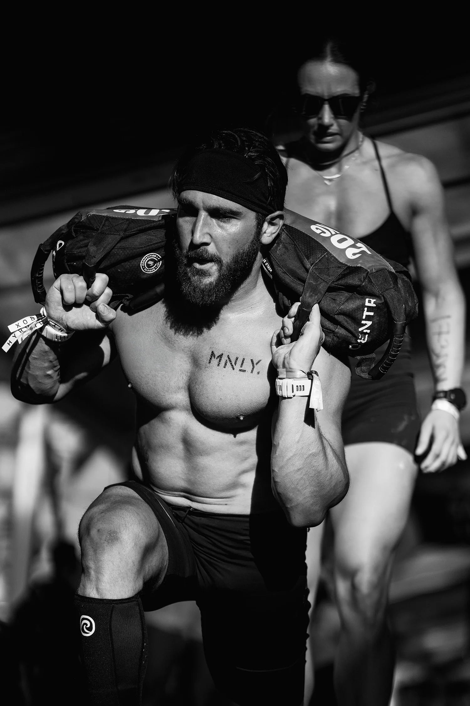 A Hyrox competitor carrying a sandbag with MNLY stenciled on his chest
