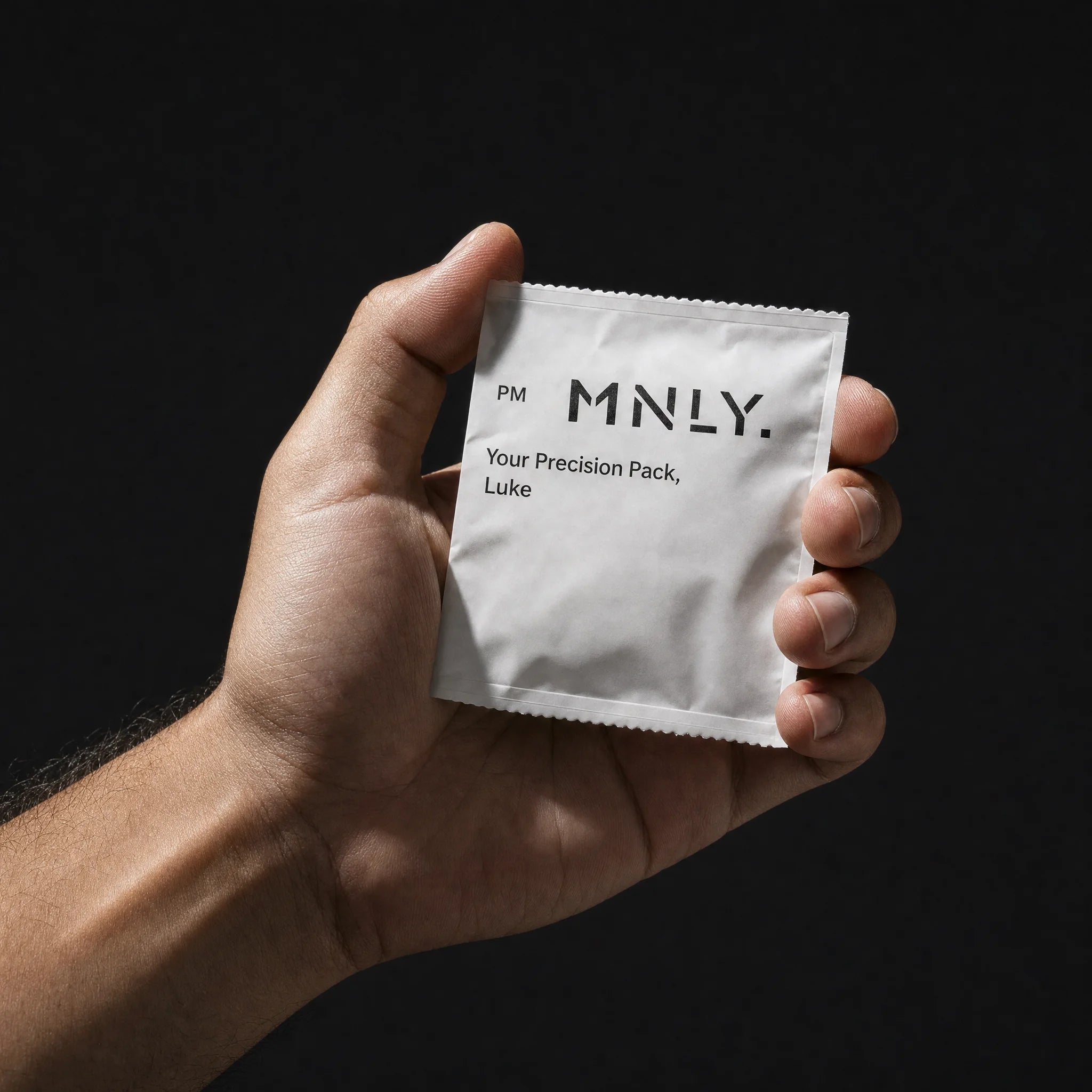 A single MNLY Precision Pack sachet held in a man's hand against a dark ground
