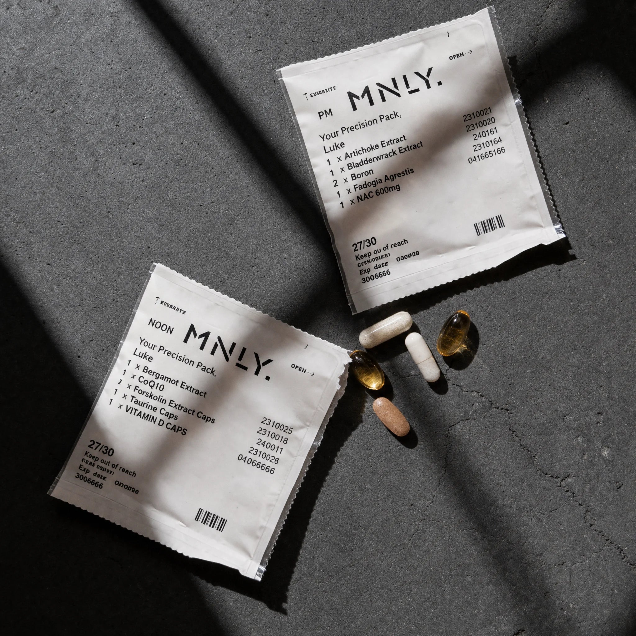 Two MNLY Precision Pack sachets on slate with loose capsules